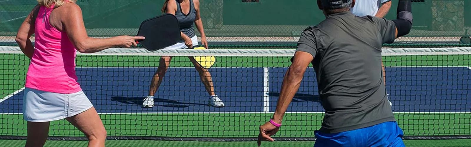 Mixed doubles pickleball match on an outdoor court in daylight