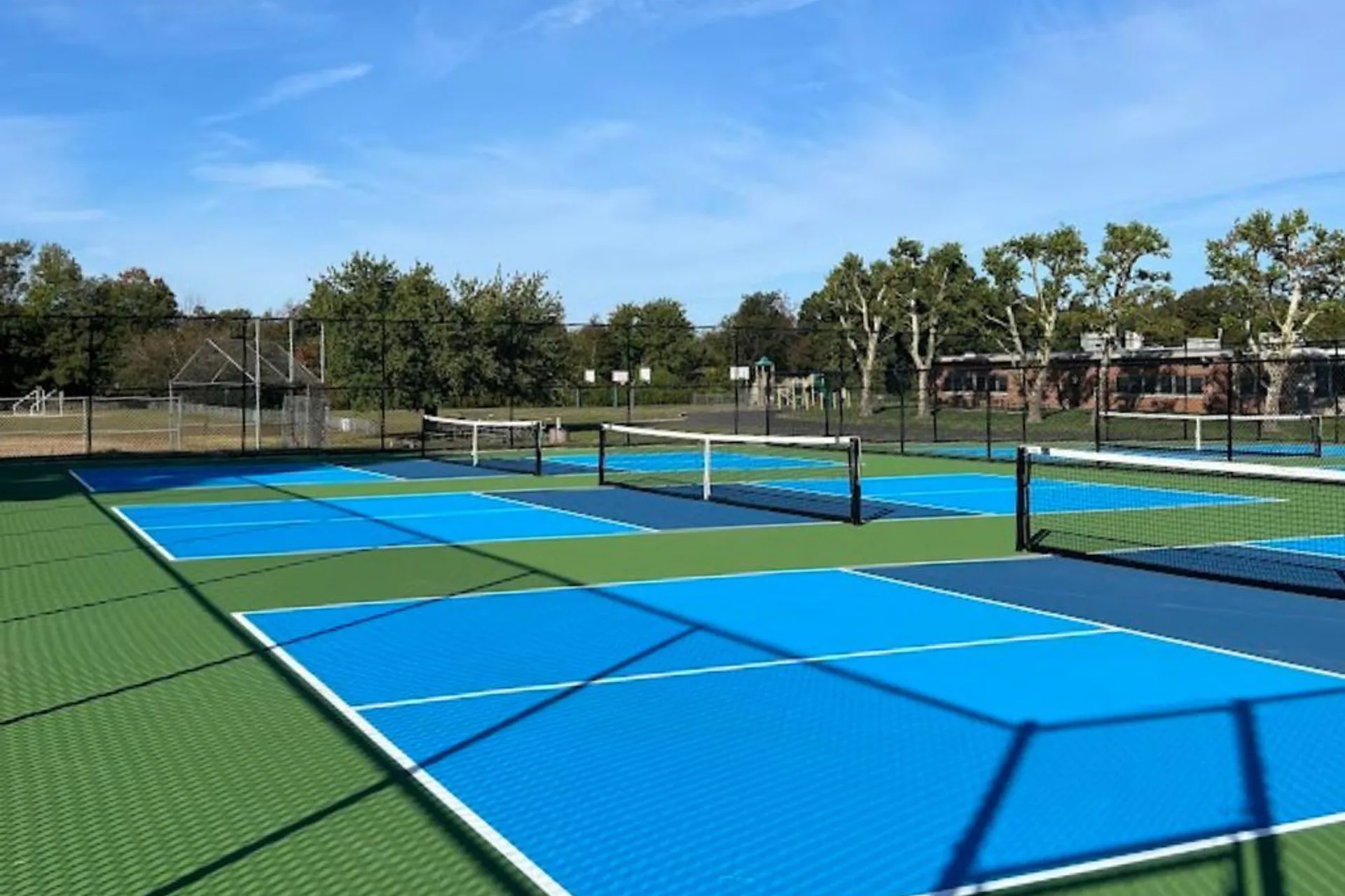 Newly resurfaced outdoor pickleball courts at a New Jersey public park, with blue playing areas, green surrounds, and nets set up